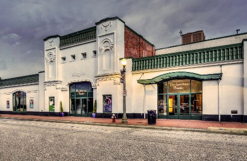 Large white theatre building with green doors, awning and accents on an empty street