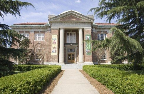 Large, stately museum with tall front pillars flanked with colorful banners and expansive sidewalk with shrubs