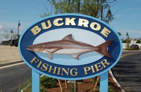 Large blue oval sign with a fish and text leading to a local fishing pier