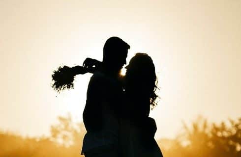 Dark silhouette of a couple embracing in front of a golden yellow and orange sky