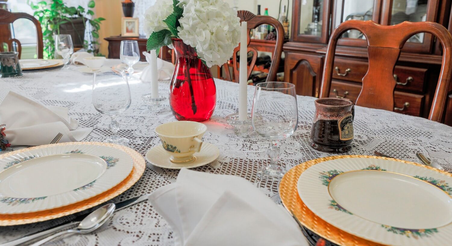 Dining table with lace tablecloth and fine china, gold charger plates and white linens