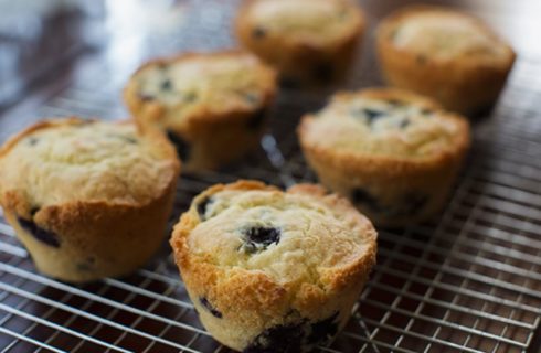 Six perfectly golden brown blueberry muffins on top of a cooling rack