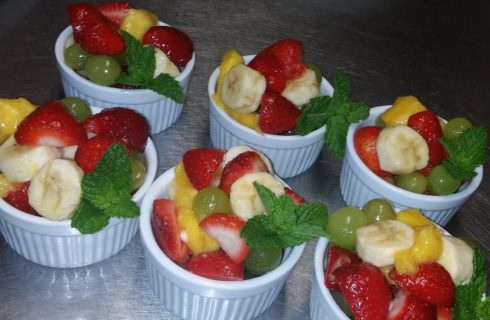 Six white ramekins filled with mixed fruit and min leaves on a silver countertop