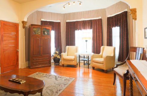 Large sitting area in front of a bay window with two chairs, side table and large armoire