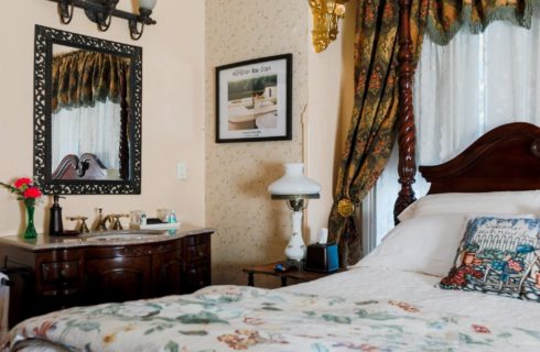 A four-poster cherry wood bed in an elegant guest room with cherry vanity and sink