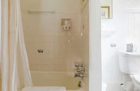 Bright white bathroom with tiled shower and tub and toilet next to a window