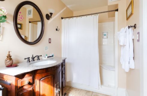 Bright bathroom with stand up shower, white curtain and dark brown vanity with sink and oval mirror