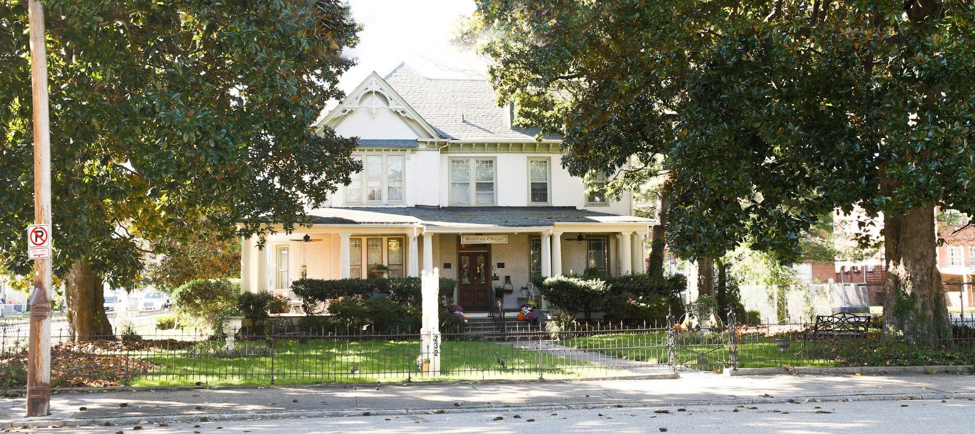 Front facing view of a beautiful white home with large front porch, white columns and wrought iron fence around yard