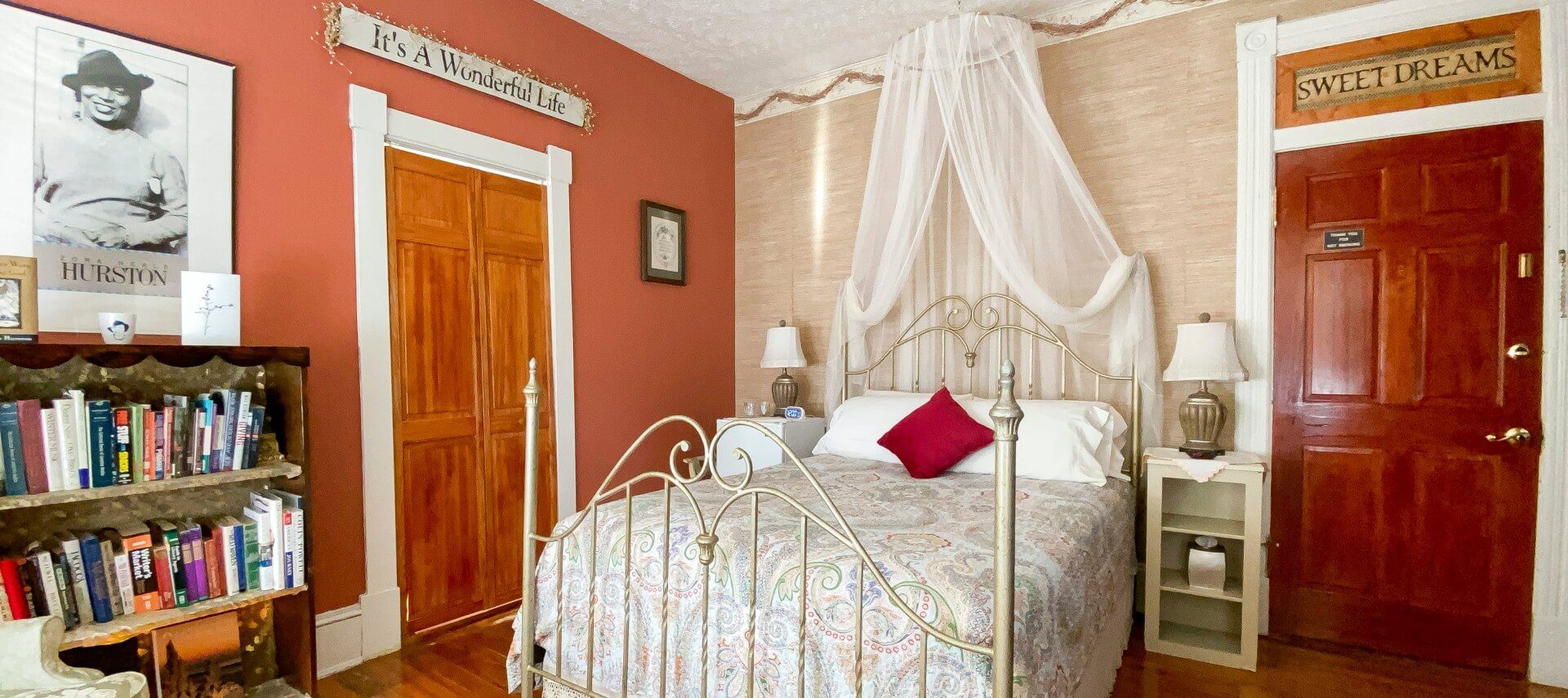 Four-poster brass-style bed with net canopy in room with bookshelf and two bedside tables