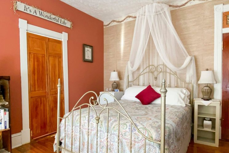 Four-poster brass-style bed with net canopy in room with bookshelf and two bedside tables