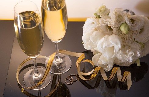 Two glasses of champagne next to a bouquet of white flowers and a curly gold ribbon