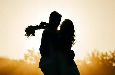 Silhouette of a man and woman hugging against a golden orange and yellow sky