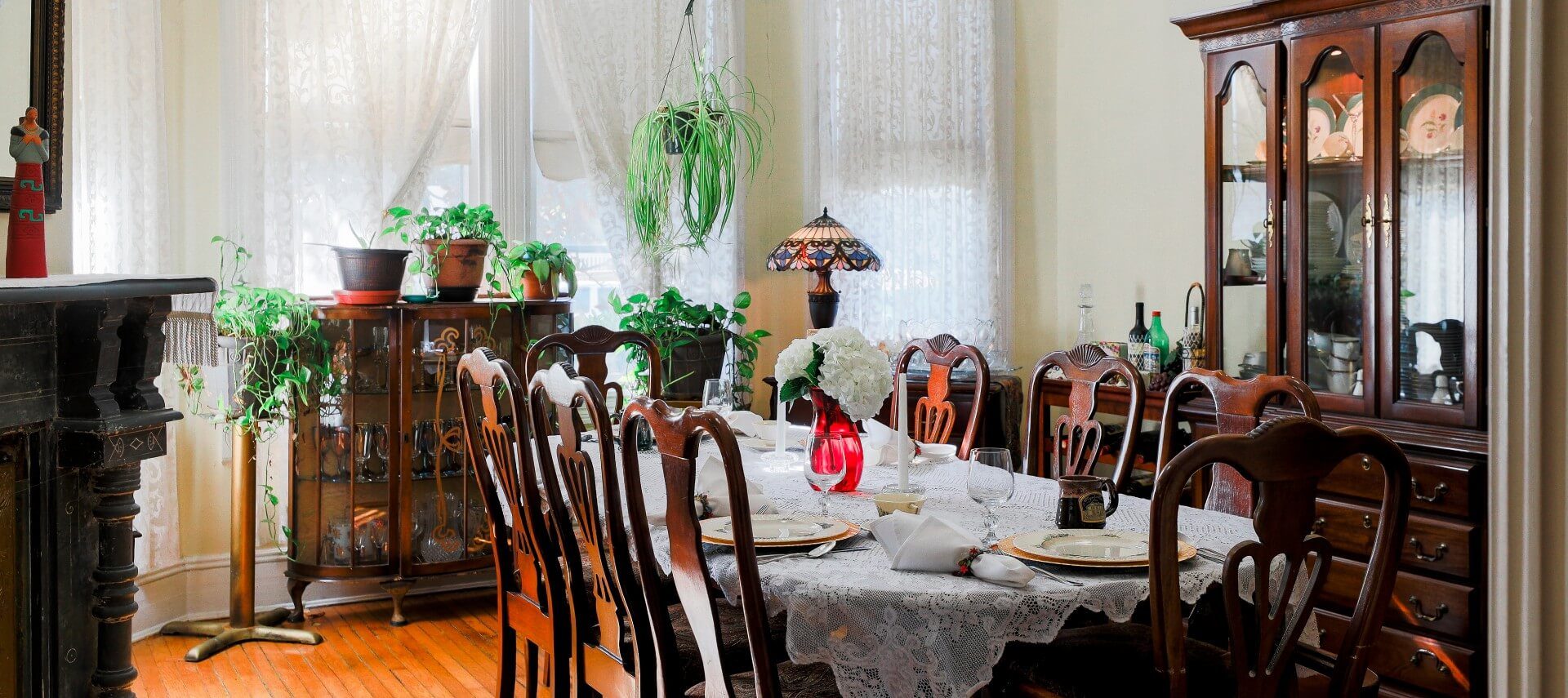 Large dining room with hutches and antique table and 8 chairs, set with lace tablecloth and fine china