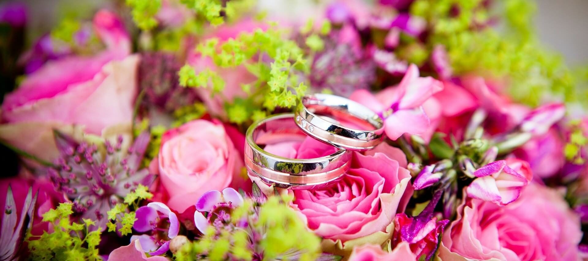 Two silver wedding rings sitting atop a bright pink and purple bouquet of flowers with green springs