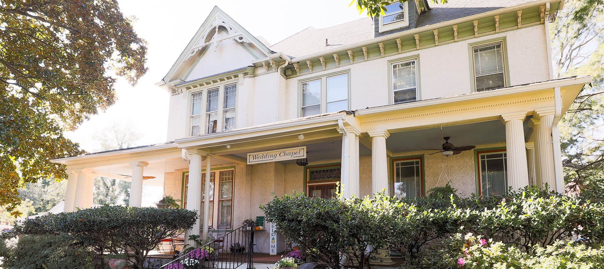 Front facade of gorgeous historic white home with large front porch with columns and green shrubs