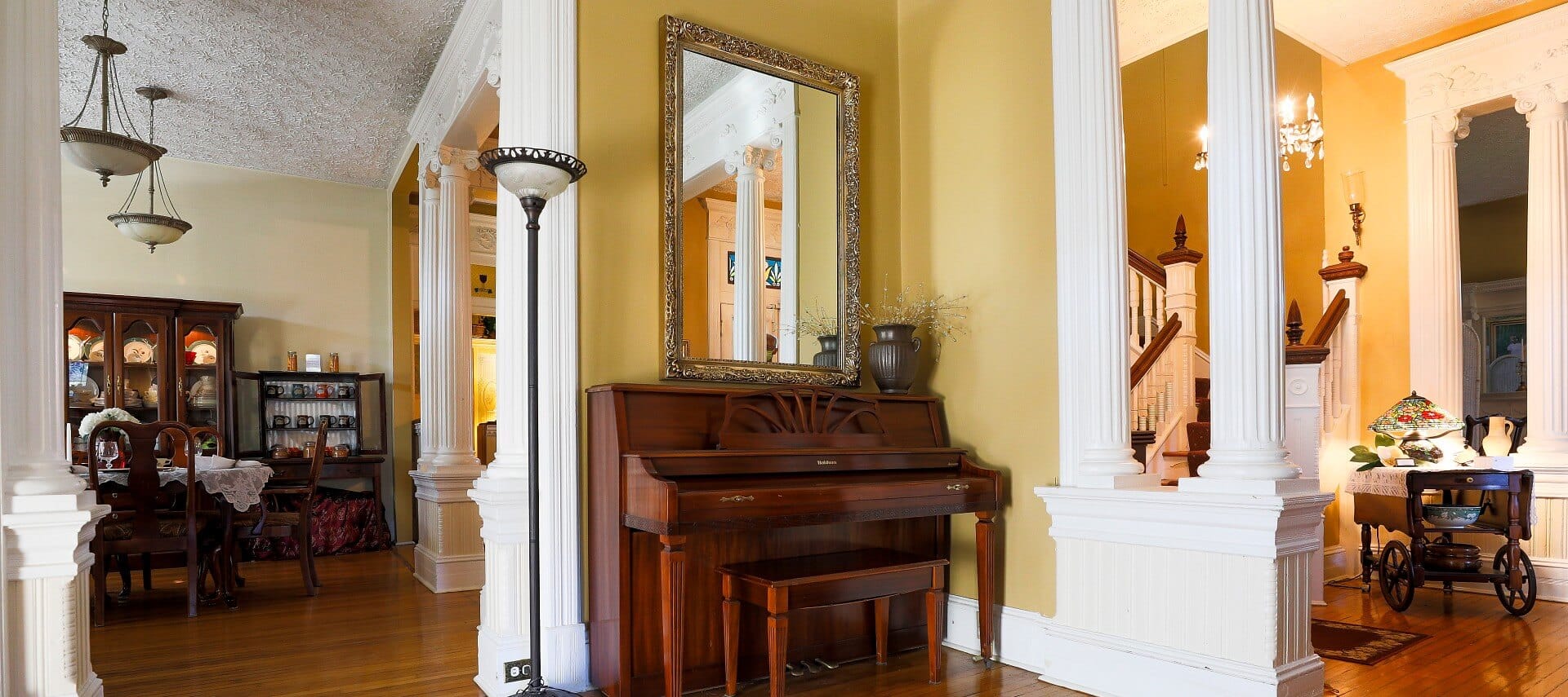Interior great room of a historic home with white columns, stairway, stand up piano and dining area
