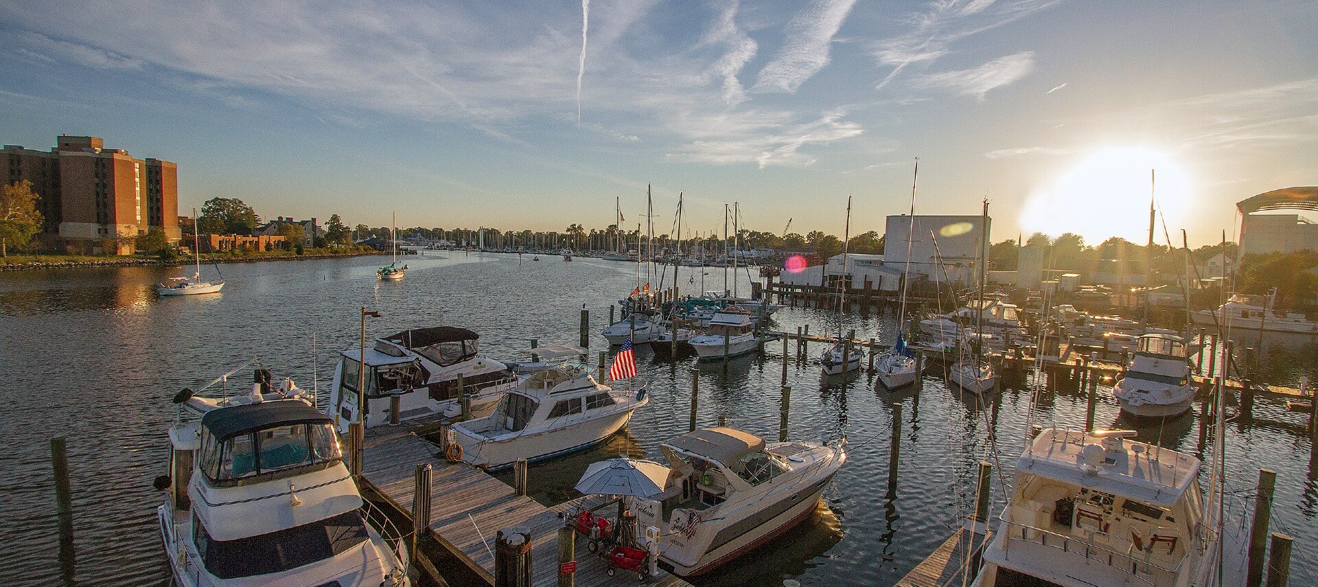 Harbor with many boats docked by decks and city buildings in the background against a blue sky