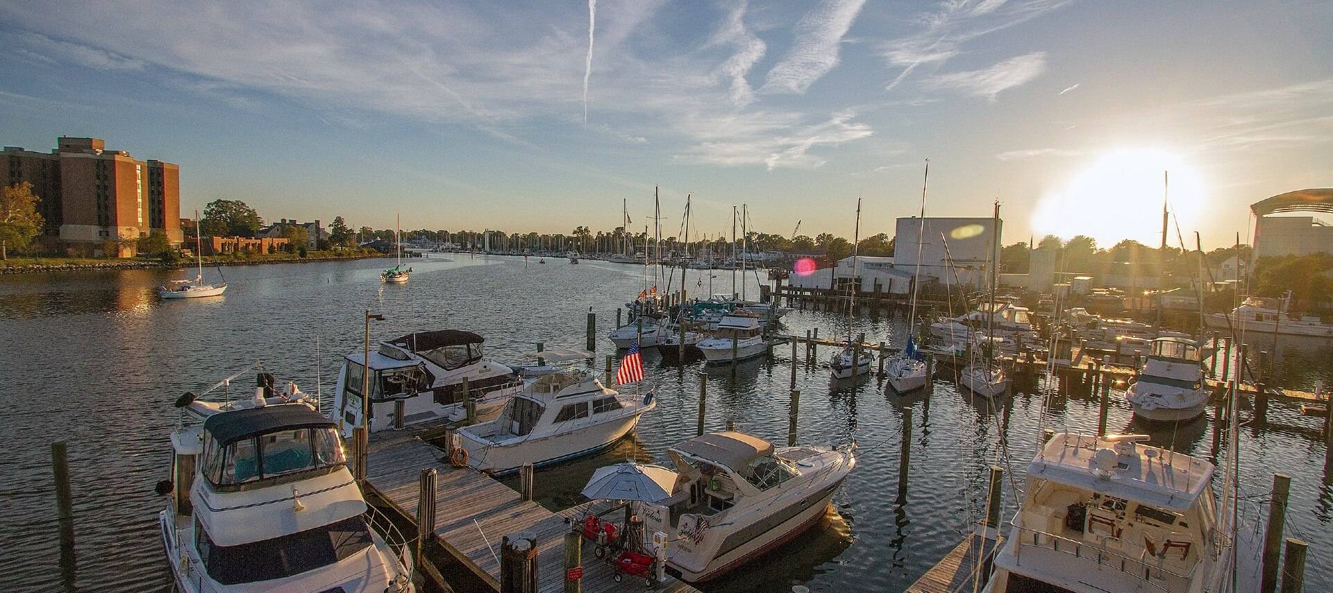 Harbor with many boats docked by decks and city buildings in the background against a blue sky
