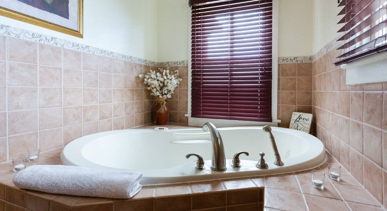 Large soaker tub in the corner of a bathroom with brown tile and a two windows with burgundy shades